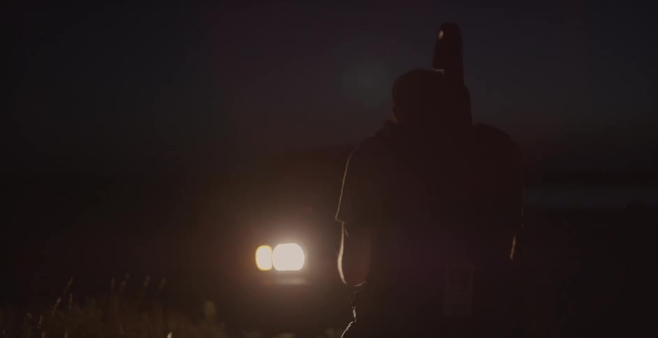 Man carrying camera equipment outside while headlights shine