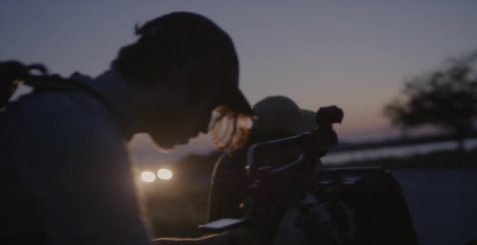 A woman is recorded by a film crew while standing in a rural area at sunset