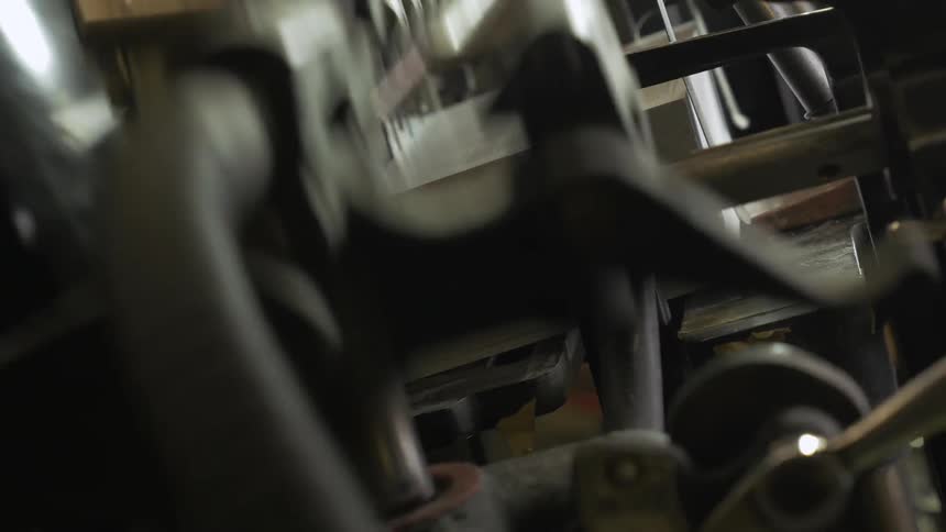 A bar on some industrial machinery moves up and down over a stack of paper