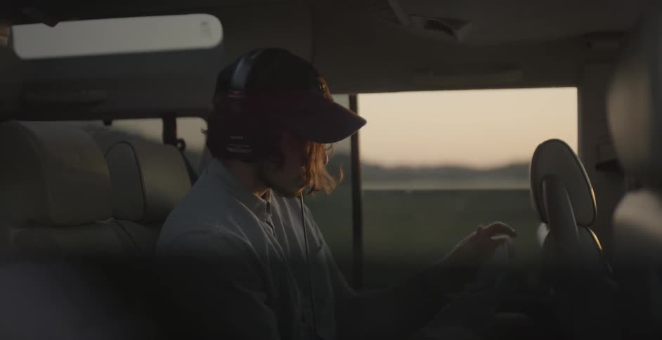 A man rides in a car and puts on headphones at sunset