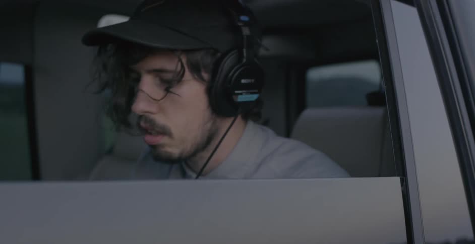 A man in a car with headphones looking down at something