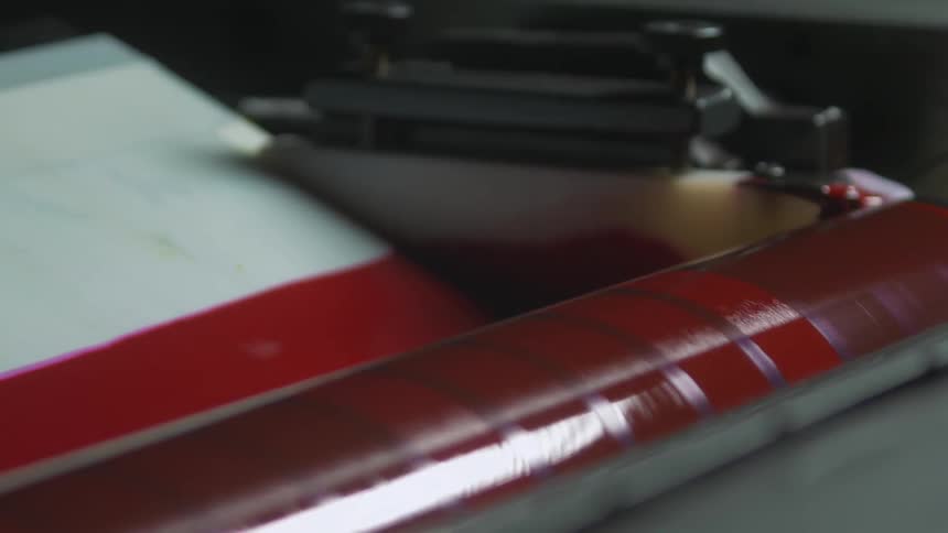 A printing press roller covered in red ink is spinning slowly