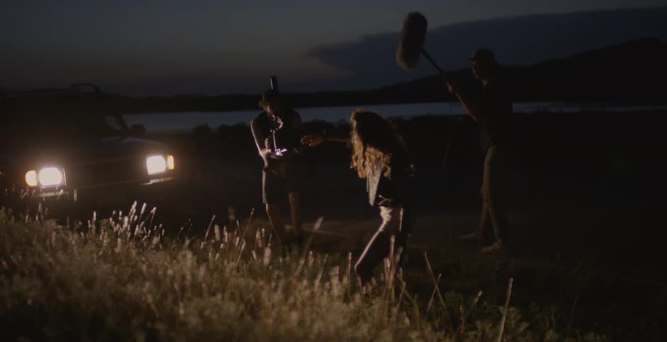 People are filming at night in front of a vehicle with headlights on