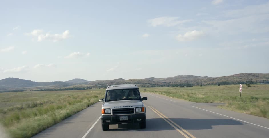 A gray land rover travels an empty road