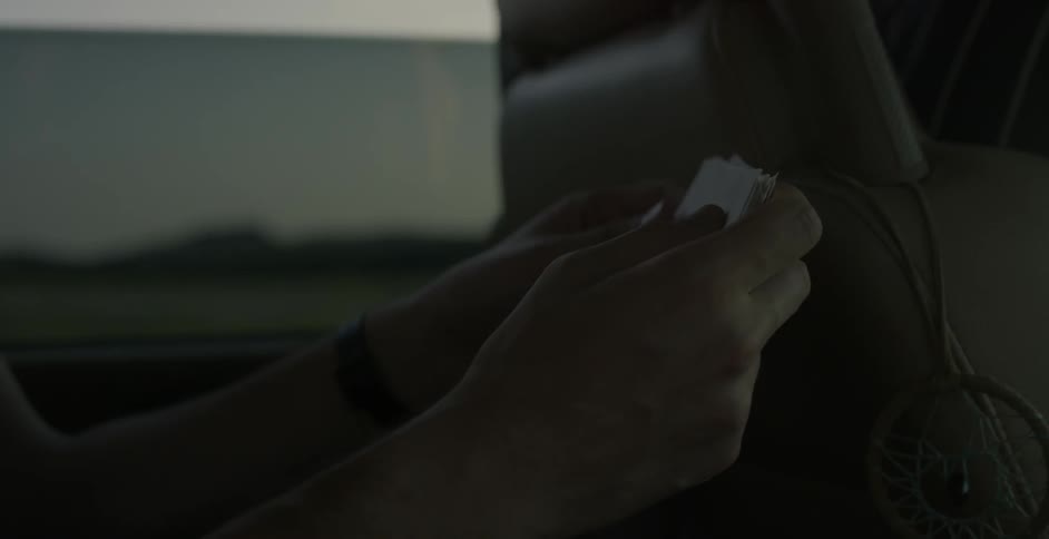 A person is looking at cue cards in the seat of a dark car