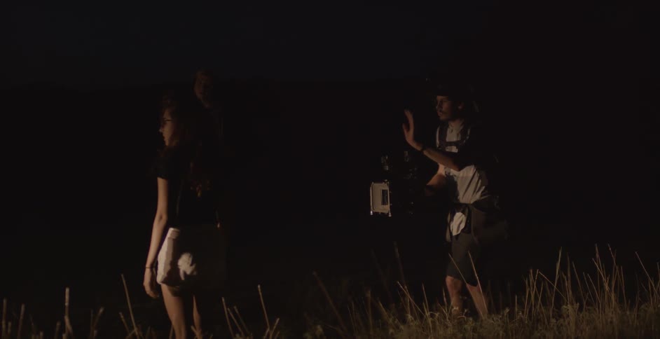 A cameraman gestures to direct action as a crew films at night
