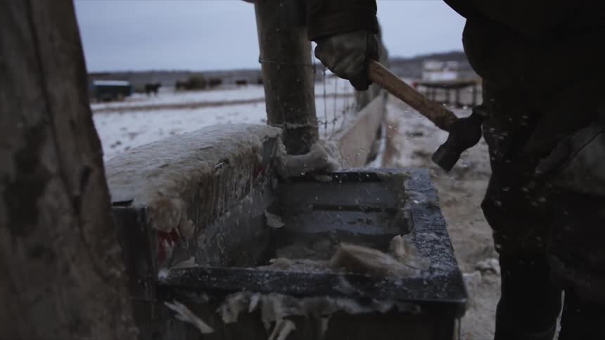 A person with a hammer knocks ice of a trough