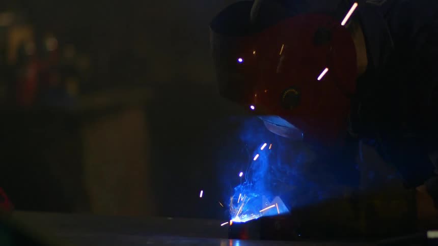 Sparks and smoke fly around a welder's mask