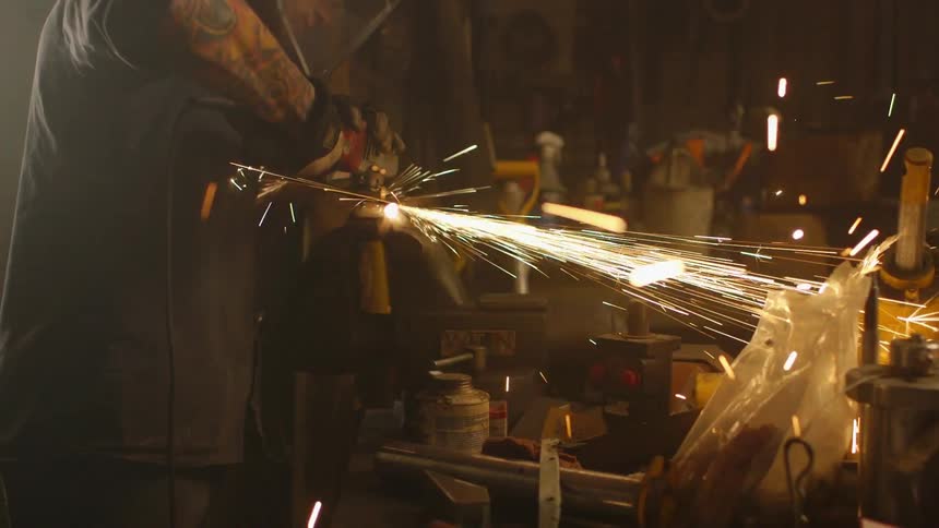 A man is grinding metal in a dark garage