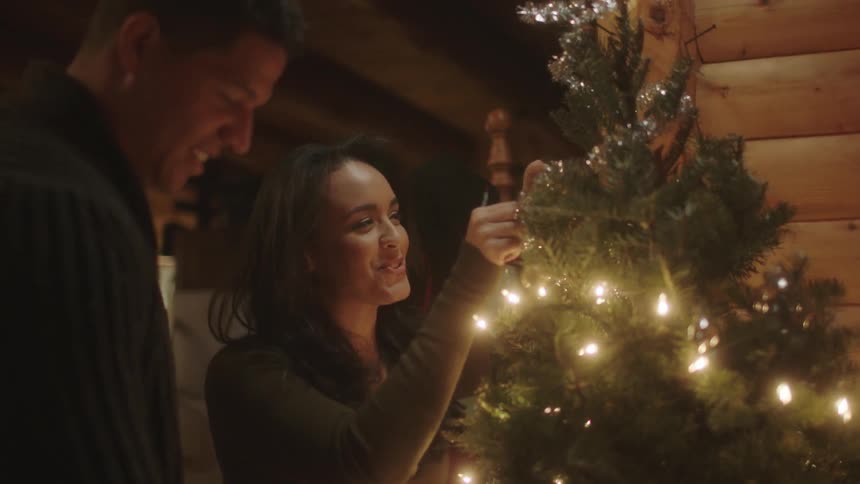 A man and woman decorate a christmas tree