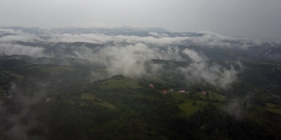 Wispy clouds and fog drift over a village and mountains