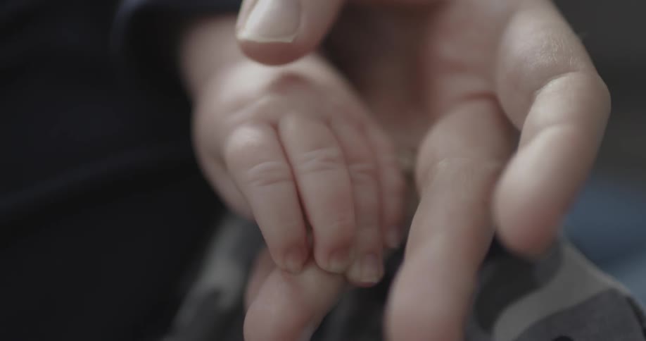 A woman is holding a baby's hand in hers