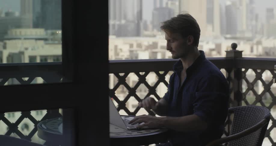 A man is sitting on a balcony working on a laptop