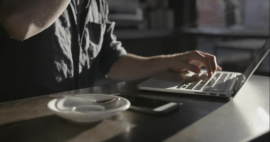 A man drinks coffee while working on his laptop