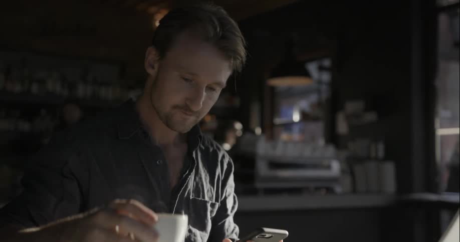 A man drinks from his mug looking at his phone