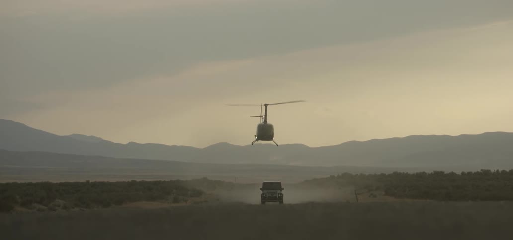 A helicopter flies over a vehicle on a dirt road