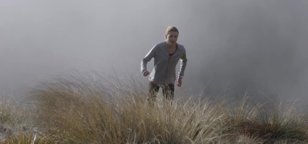 Woman runs through tall weeds and fog