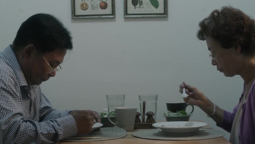 An elderly couple eat together at a small table