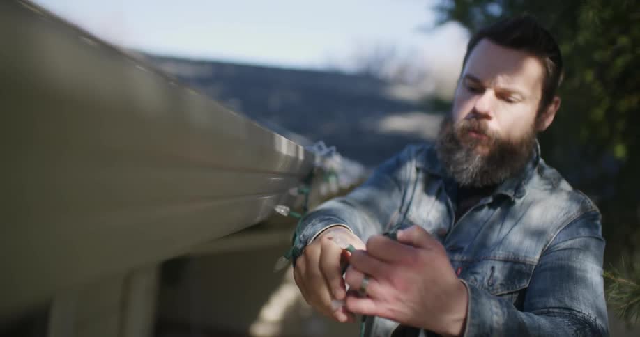A bearded man hangs christmas lights