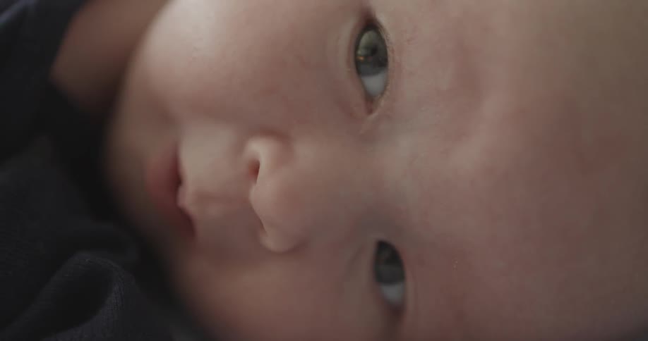 A baby is moving its mouth and looking about as it is lying down