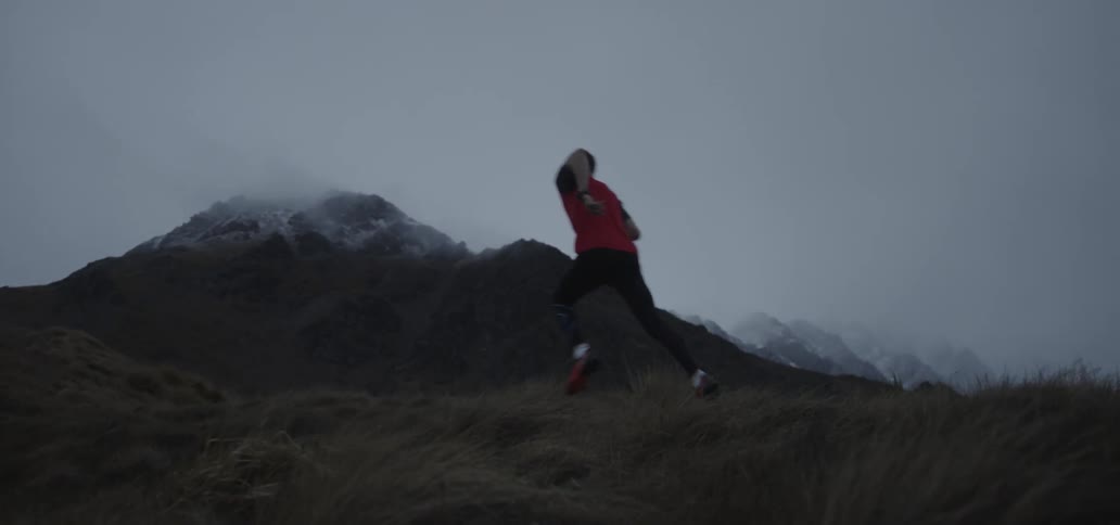 A man in a red shirt runs up a scrubby hill