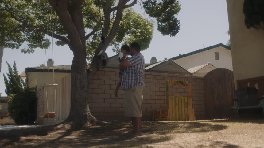 A man is holding and playing with his son in their backyard