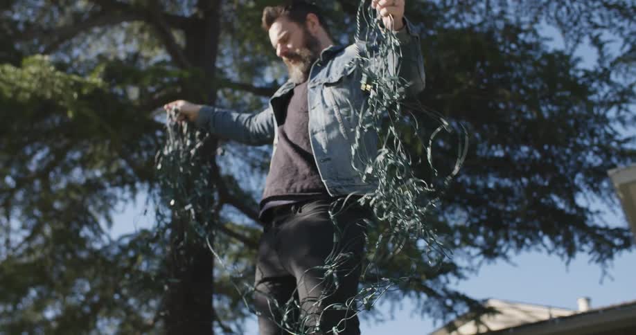 A man is trying to untangle a bunch of christmas lights