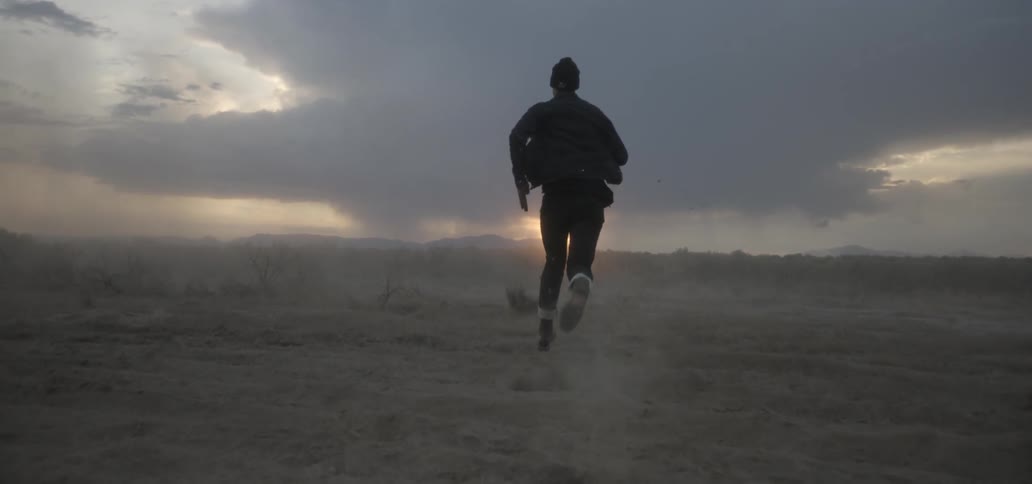 A man is running down a long field at sunset