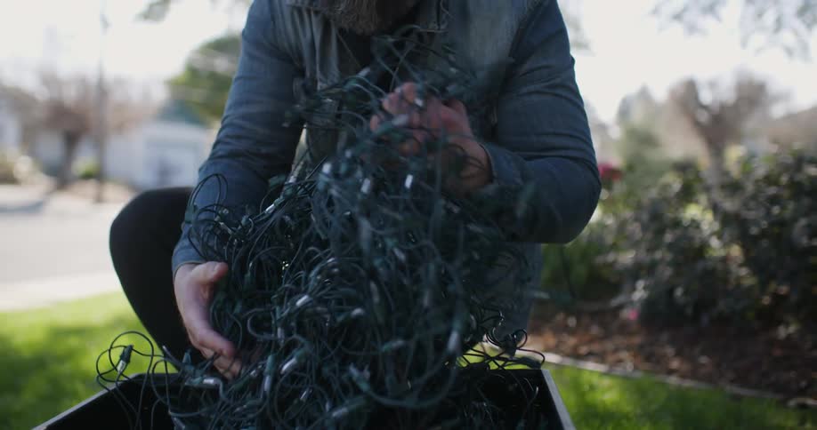 A man pulls christmas lights from a crate in a front yard