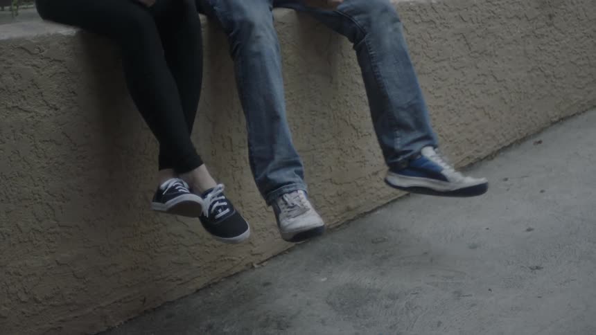 Two people sitting on a concrete ledge swinging their legs