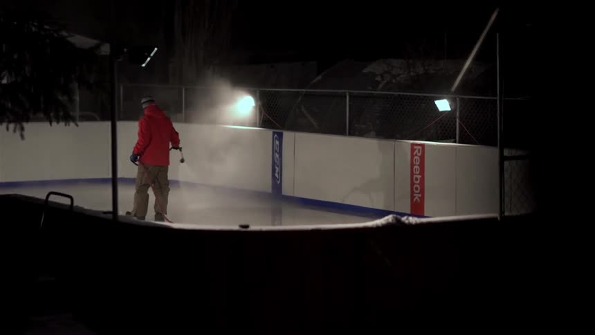 A man sprays an ice skating rink with water