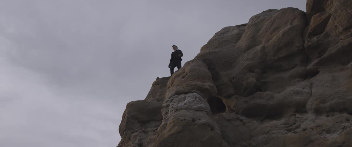 A person on top of a large rock with the cloudy sky in the back