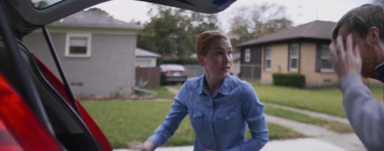 Man and woman pack a car trunk together in a quiet neighborhood
