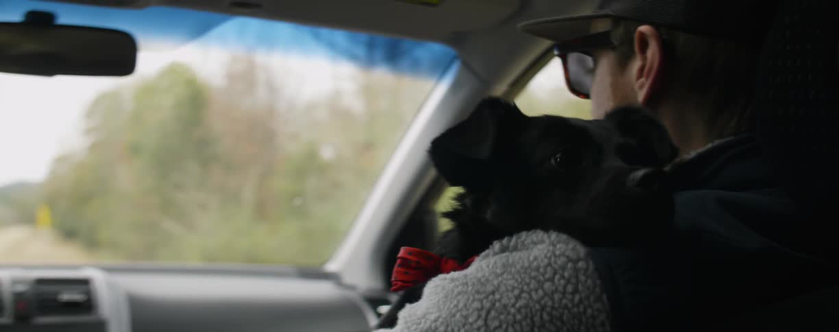 Man riding in a car holding a black dog