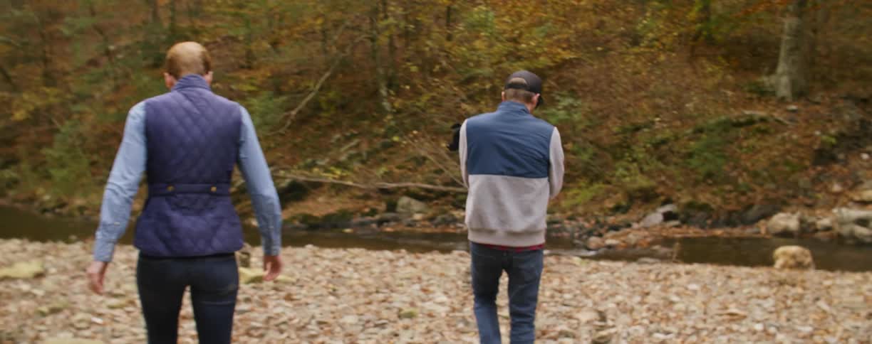 A couple with a dog hike toward a stream on an autumn day