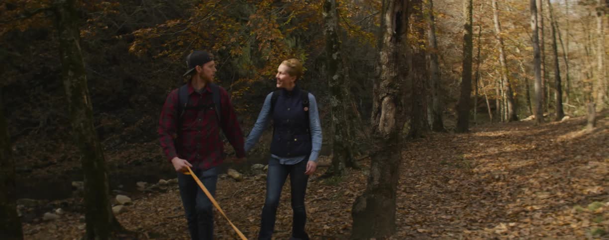 Man and woman walk in the woods with a small dog