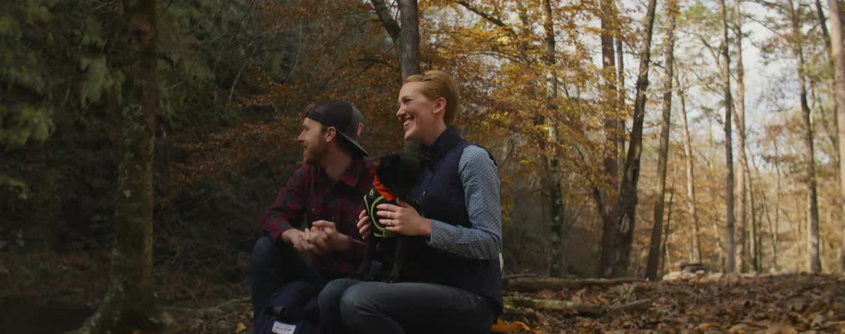 A couple of people and a dog sitting in the woods talking and laughing