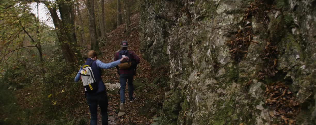 Couple hiking through the woods carrying backpacks and a dog