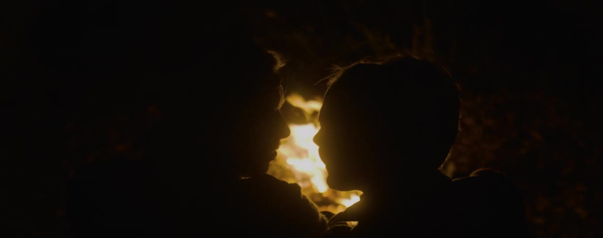 Man and woman sit close talking next to a fire