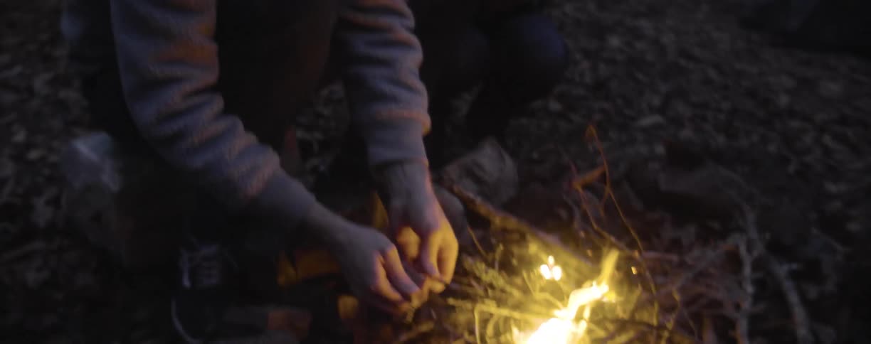 A couple kneel in front of a a small campfire