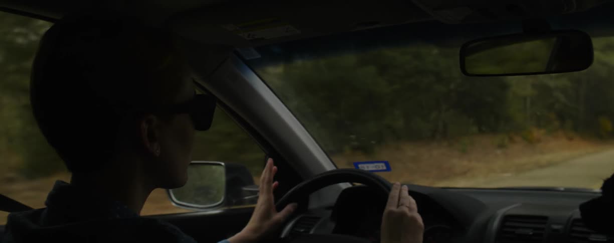 A person drives a car while singing and tapping fingers on the wheel