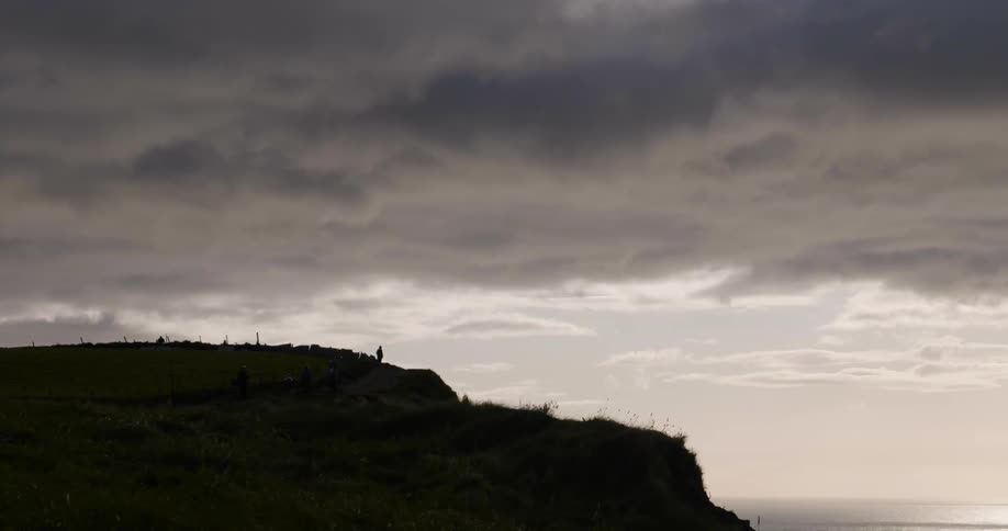 A man walks atop a mountain under gray clouds