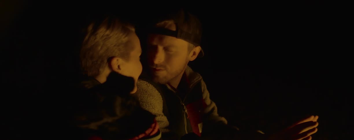 A man and woman cuddle and kiss near a fire at night