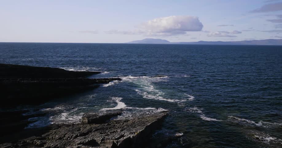 An ocean with rocks along the edge on a sunny day
