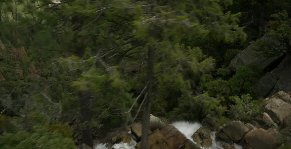 A moving view of a mountains, water and trees with the water flowing down
