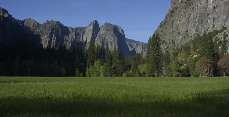 Shadows creep across a field in a valley in yosemite
