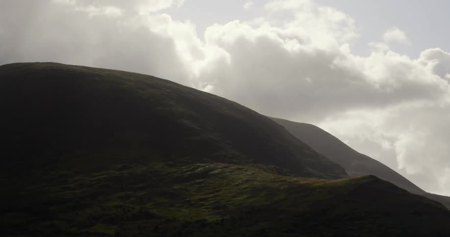 White clouds float over green hills