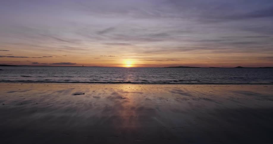 Waves roll onto beach sands at sunset