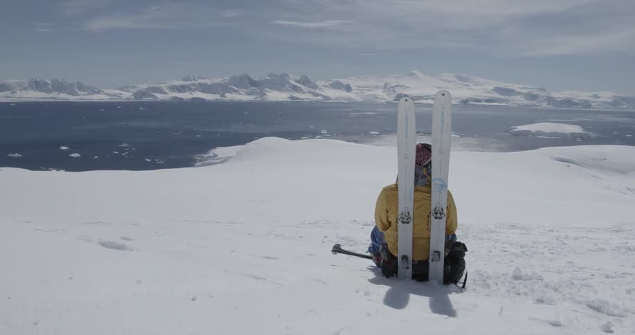 A person sitting in the snow looking out over landscape with skis propped up behind them