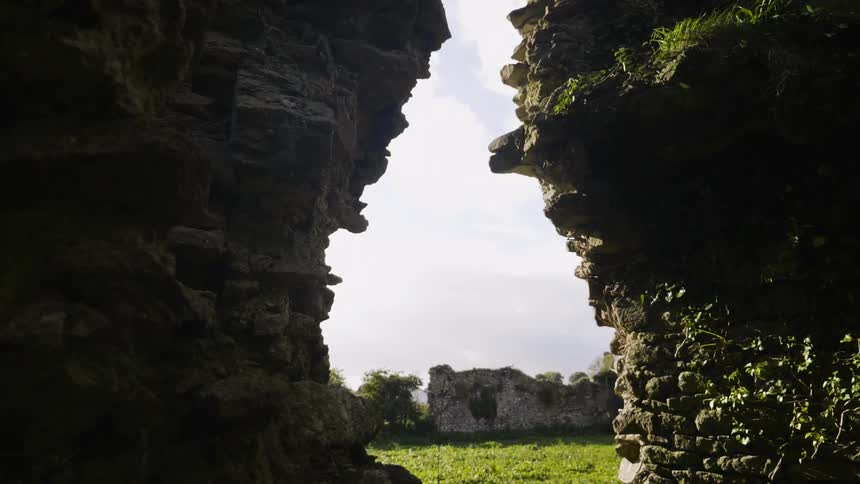 A break in an ancient stone wall reveals a cloudy sky and ruins